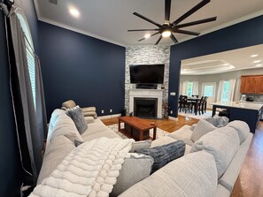 A modern living room with a fireplace, a ceiling fan, and a dining area in the background. - Spacious 3BR/3BA Home Patio, Yard & Garage (Kathleen)
