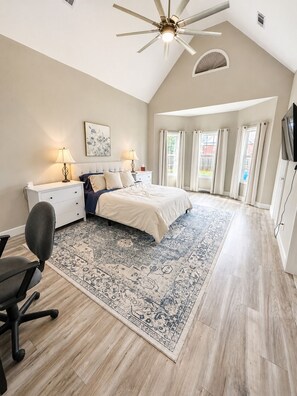 A bedroom with a bed, desk, chair, ceiling fan, and a large window with curtains. - Spacious 3BR/3BA Home Patio, Yard & Garage (Kathleen)