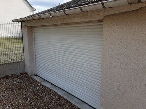 A closed roller shutter garage door with a concrete base and a metal fence in the background. - A FAMILY-FRIENDLY LONGÈRE IN SOLOGNE, AMIDST THE CASTLES AND NEAR THE BEAUVAL ZOO (Cour-Cheverny)