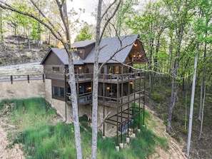 A multi-story cabin with a balcony, surrounded by trees. - Family Retreat w/ Indoor Pool - Sleeps 20 (Sevierville)