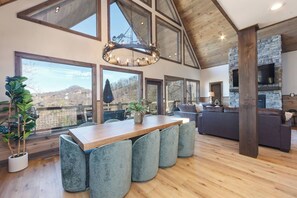 A spacious living area with a wooden dining table, grey upholstered chairs, a large chandelier, and a stone fireplace. - Family Retreat w/ Indoor Pool - Sleeps 20 (Sevierville)