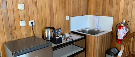 Una kitchenette compacta con refrigerador GE, un lavamanos, una cafetera y un extintor.