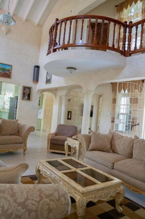 A spacious living area with a high ceiling, a wooden staircase, and a view of the kitchen. - Spacious 5-bedroom house in soothing Bridgetown with AC (Bridgetown)
