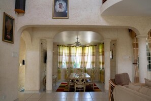 A dining area with a table and chairs, a ceiling fan, and a window with curtains. - Spacious 5-bedroom house in soothing Bridgetown with AC (Bridgetown)