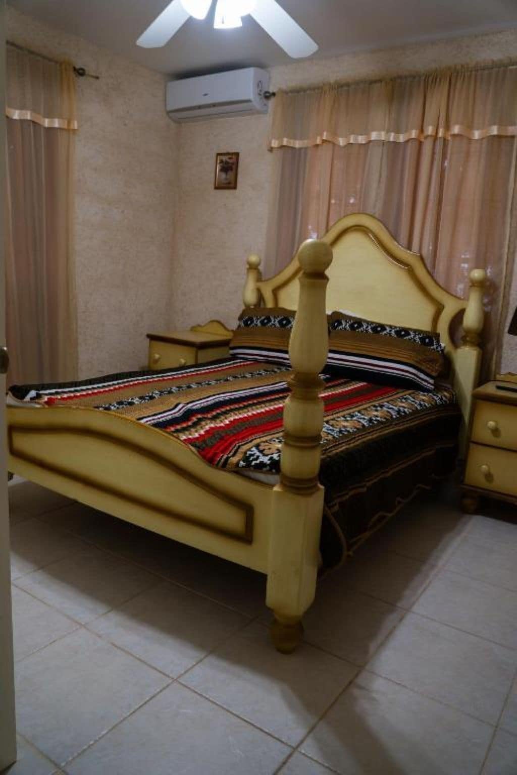 Ein Schlafzimmer mit einem hölzernen Bett, einem Nachttisch, einer Kommode und einem Deckenventilator.