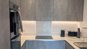 Eine moderne Küche mit grauen Schränken, einem eingebauten Ofen, einer Kaffeemaschine und einem Wasserkocher auf der Arbeitsplatte.