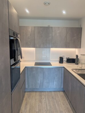 A modern kitchen with grey cabinets, a built-in oven, a coffee maker, and a kettle on the countertop. - Modern Zone 2 Flat - 10 mins to London Bridge (London)