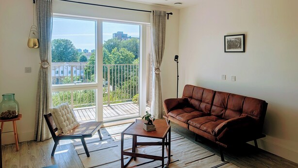 Ein Wohnzimmer mit braunem Ledersofa, einem Holztisch, einem Sessel und Blick durch eine Glastür auf einen Außenbalkon.