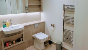 Ein Badezimmer mit Waschbecken, Toilette, Spiegel, Regalen und einem Handtuchhalter.