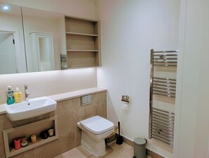 A bathroom with a sink, toilet, mirror, shelves, and a towel rack. - Modern Zone 2 Flat - 10 mins to London Bridge (London)
