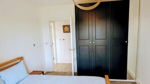 Ein Schlafzimmer mit einem Bett, einem Holz-Kopfteil, einem schwarzen Kleiderschrank und einer weißen Tür zu einem anderen Raum.