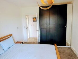 A bedroom with a bed, a wooden headboard, a black wardrobe, and a white door leading to another room. - Modern Zone 2 Flat - 10 mins to London Bridge (London)