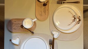 A table set with a white plate featuring a deer design, a white mug, a knife, a fork, and a spoon.