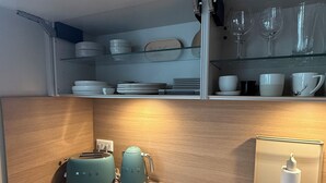 A kitchen with a wooden countertop, a toaster, a kettle, a sink, and glassware on shelves.