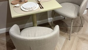 A dining area with a table set for two, a chair, and a window with blinds.