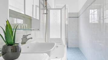 Ein modernes Badezimmer mit einer großen, weißen Badewanne, einer Duschkabine aus Glas und einer Topfpflanze.