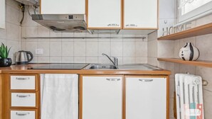 Una cucina con mobili bianchi, una cappa in acciaio inossidabile, un lavello e un termosifone a parete.