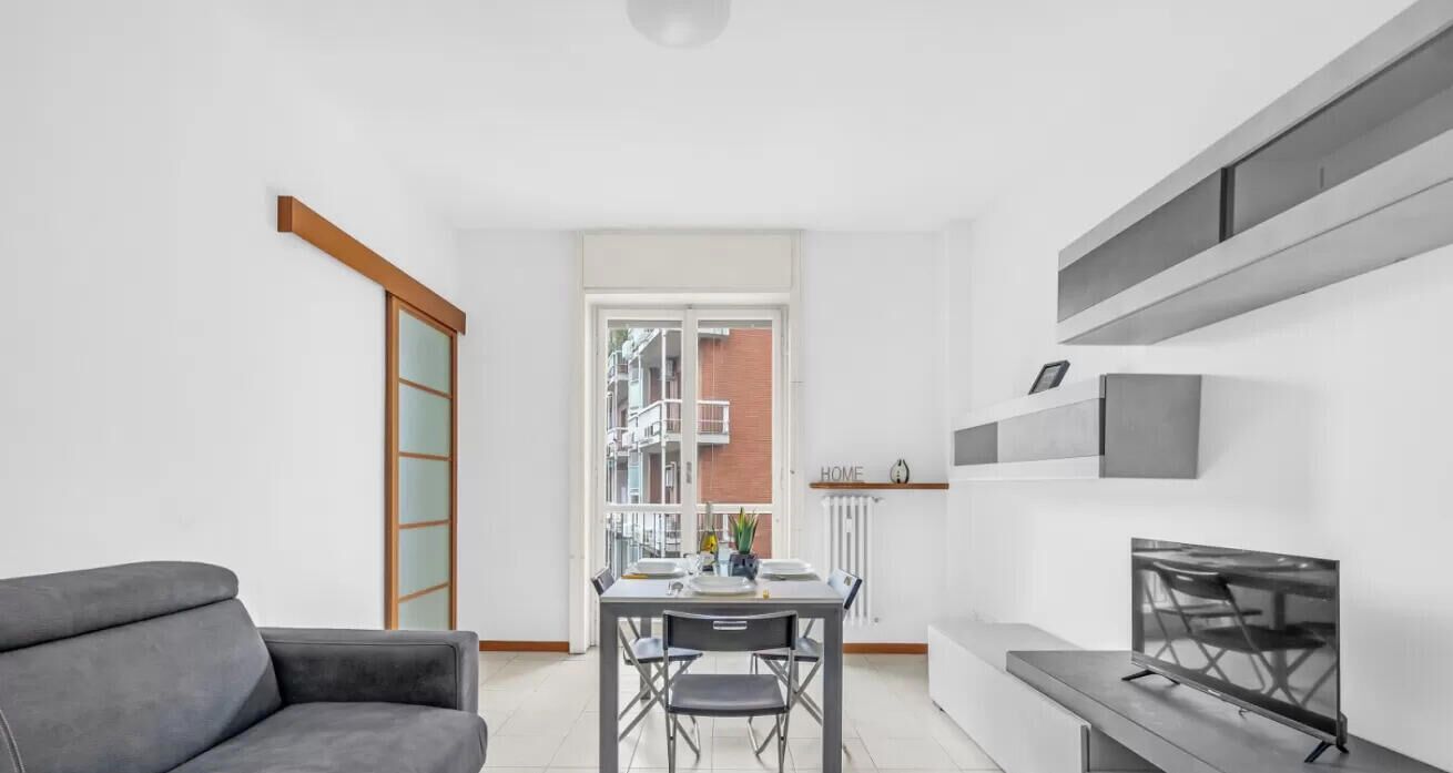 Ein modernes Wohnzimmer mit einem grauen Sofa, einem Esstisch mit Stühlen und einem Fernseher auf einem Lowboard.