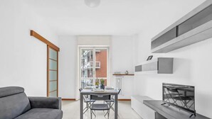 Un soggiorno moderno con un divano grigio, un tavolo da pranzo con sedie e una TV su un mobile.