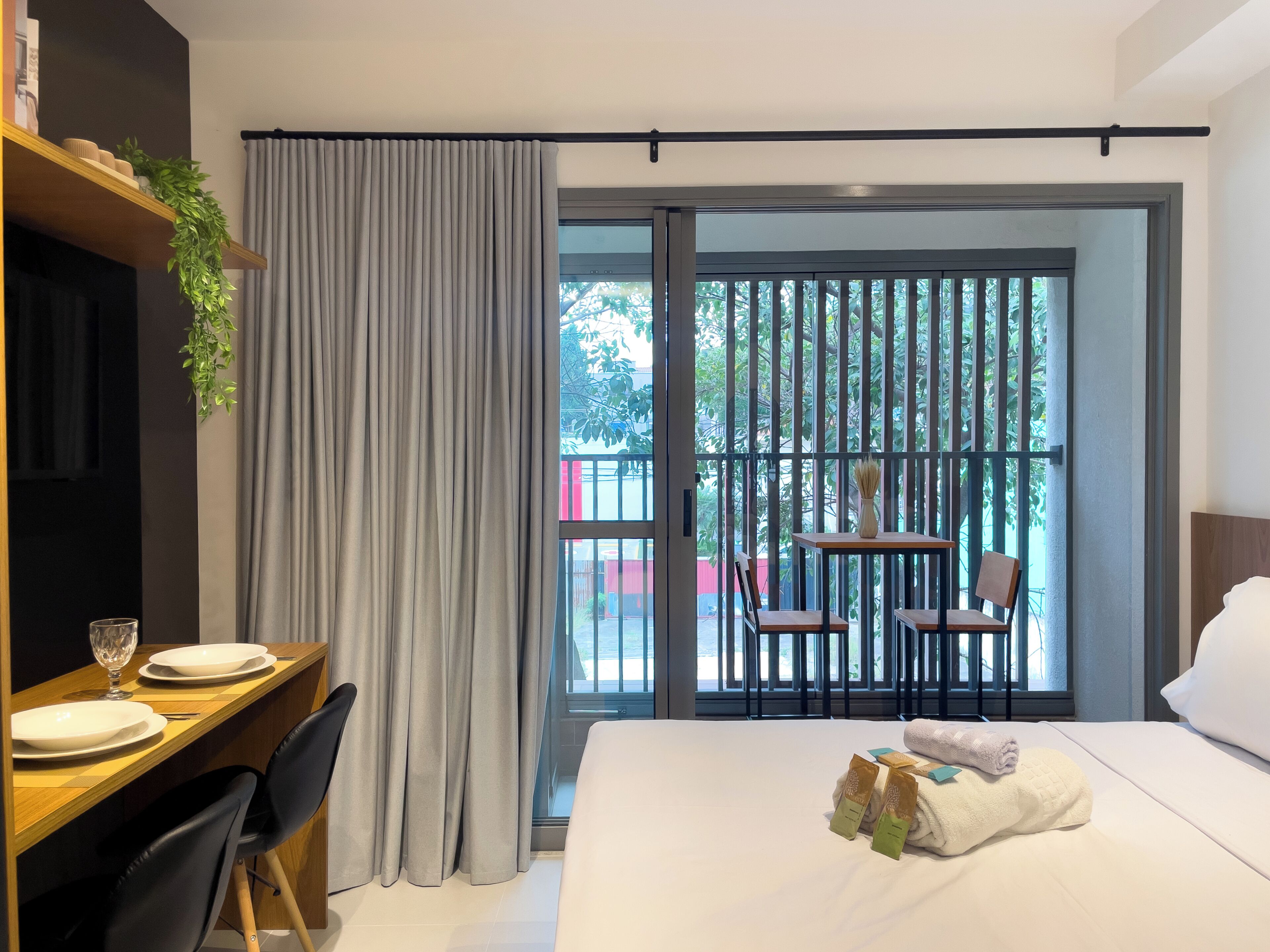 Een hotelkamer met een bed, een bureau met stoelen, een eettafel met borden en een glas, en een balkon met een tafel en stoelen.