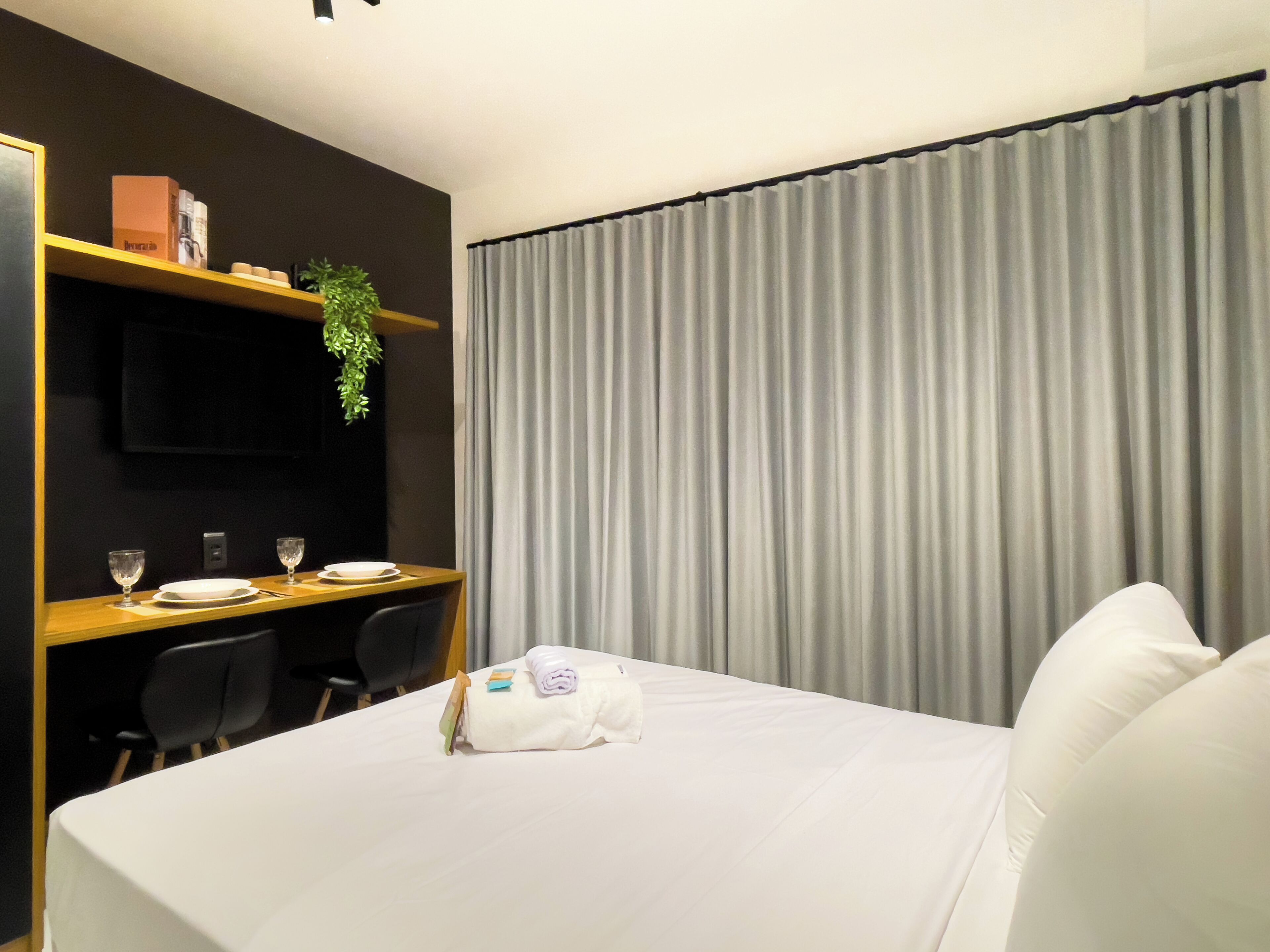 Een hotelkamer met een bed, een bureau met stoel, een televisie en een gordijn.