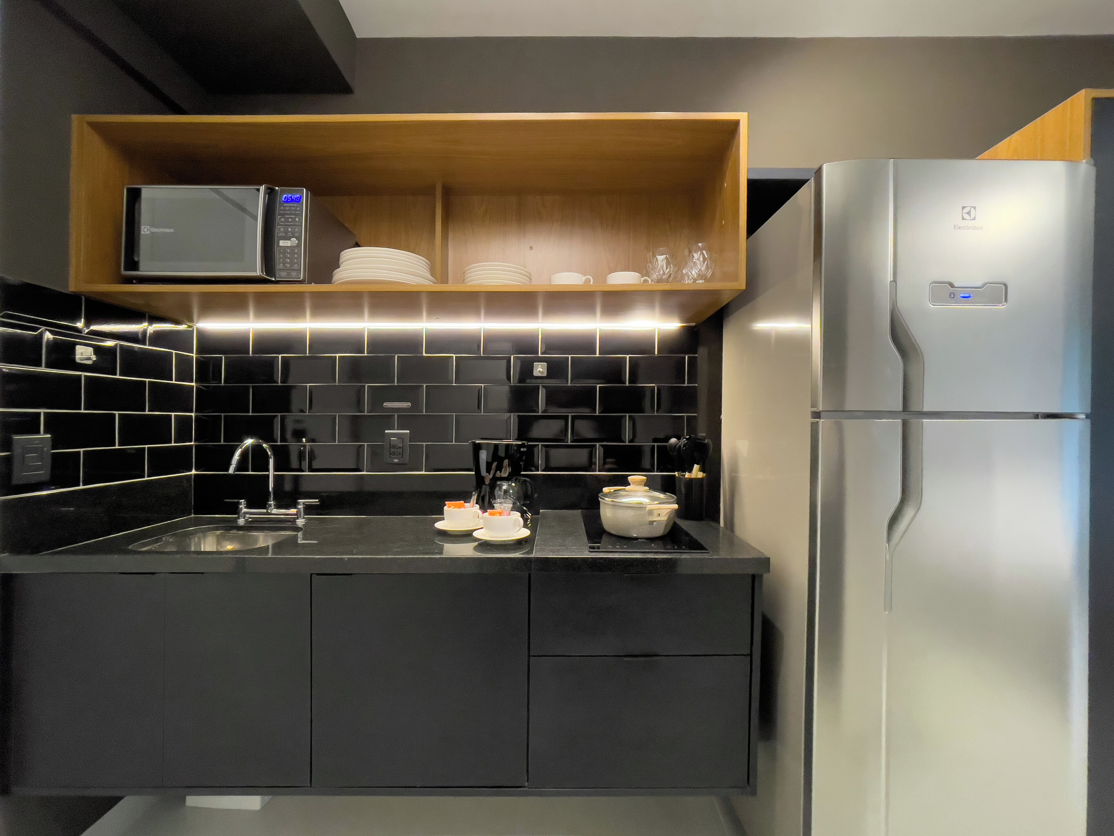 A modern kitchen with a microwave, stainless steel refrigerator, and black tiled backsplash.