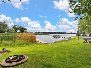 A lakeside property with a dock, grassy area, and a fire pit.