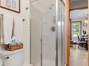 A bathroom with a glass shower enclosure, a toilet, and a wicker basket on the toilet. - Lakefront Cabin - Paddleboat, Paddleboards & Fishing Dock Included. Pet friendly (Lindstrom)