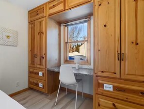 A kitchen with wooden cabinets, a window with a view, a white chair, and a countertop.
