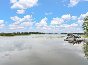 A calm lake with a dock and a boat, surrounded by greenery and a clear sky.
