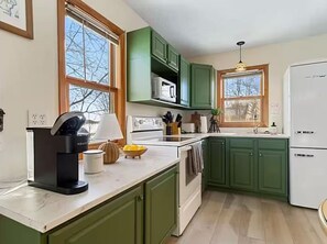 A kitchen with green cabinets, a white refrigerator, and a window with a view of trees. - Lakefront Cabin - Paddleboat, Paddleboards & Fishing Dock Included. Pet friendly (Lindstrom)