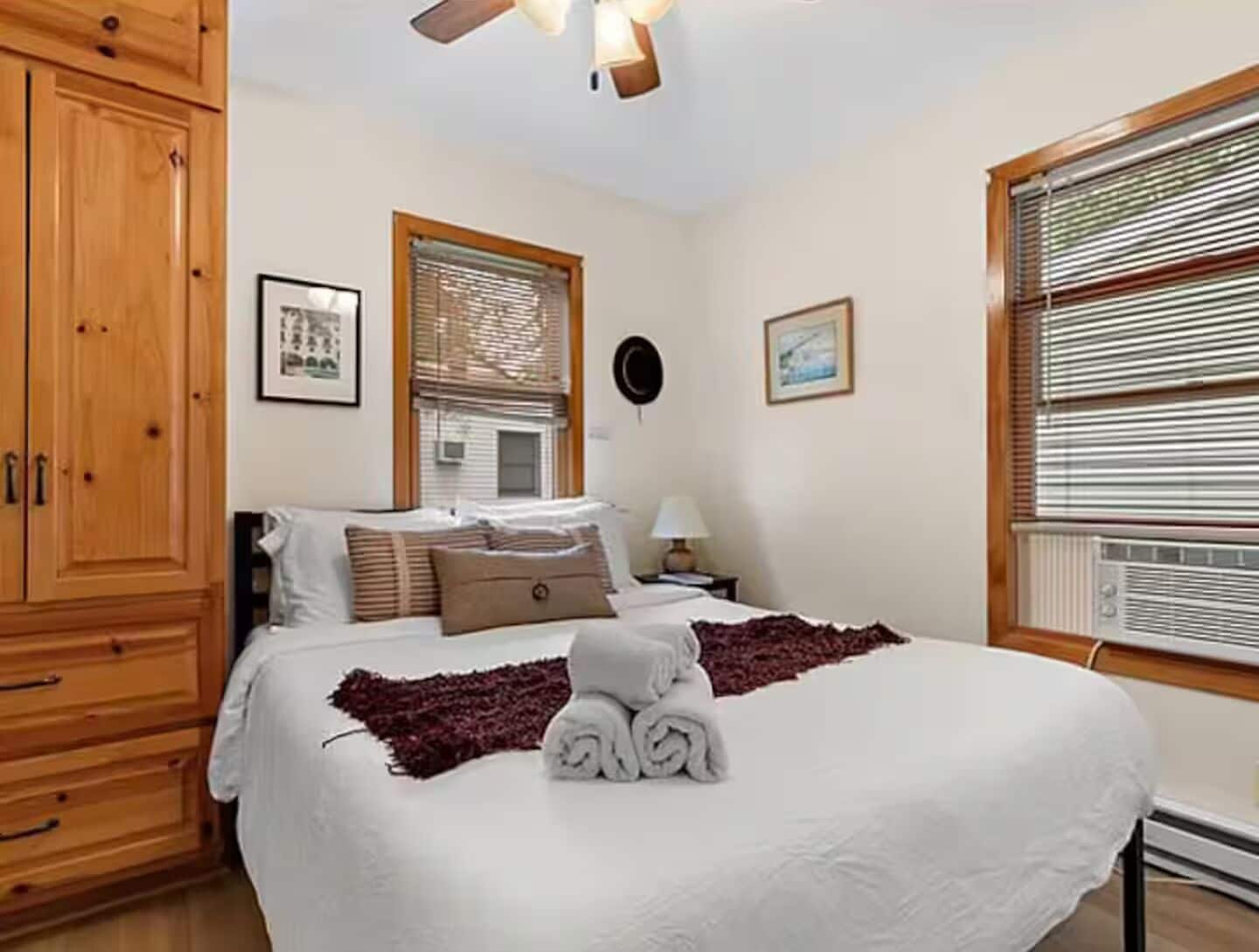 Une chambre d’hôtel avec un lit, une armoire en bois, une fenêtre avec des stores et un ventilateur de plafond.