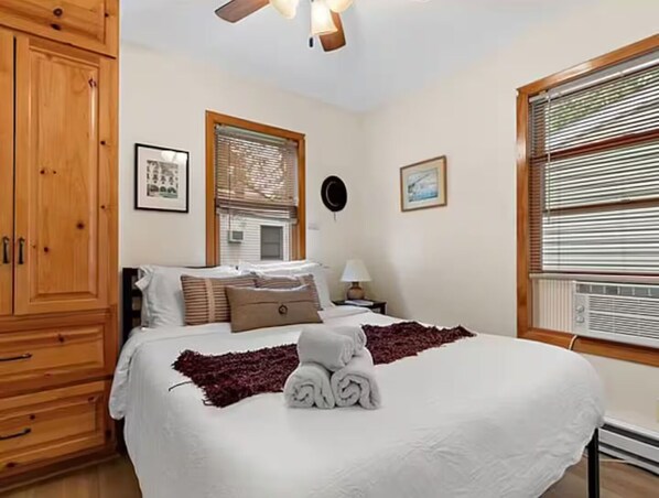 A hotel room with a bed, wooden wardrobe, window with blinds, and a ceiling fan.