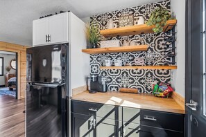Une cuisine moderne avec un réfrigérateur noir, des étagères en bois et un crédence décorée.