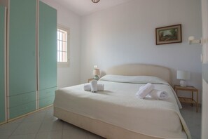 Une chambre à coucher avec un lit, une armoire, une fenêtre, une table de chevet avec une lampe et un tableau au mur.