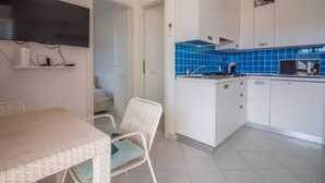 Een keuken met witte kastjes, blauwe tegels, een magnetron, en een eethoek met een tafel en stoelen.