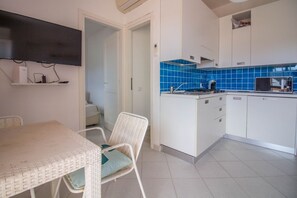 A kitchen with white cabinets, blue tiles, a microwave, and a dining area with a table and chairs. - GuestHost - Golfo Aranci Sunny Retreat Apartment with Terrace! (Golfo Aranci)