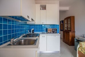 Une cuisine de taille réduite, équipée d’une cuisinière à gaz, d’un évier et de meubles blancs.