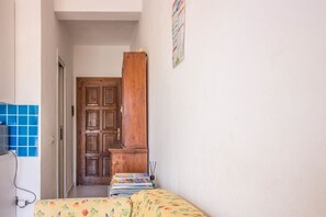 A narrow hallway with a wooden door, a bed with floral bedding, and a wall-mounted picture. - GuestHost - Golfo Aranci Sunny Retreat Apartment with Terrace! (Golfo Aranci)