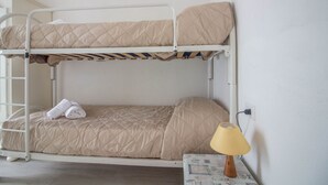 Een stapelbed met een gebonden matras, een paar opgevouwen handdoeken en een bedlamp op een tafeltje.
