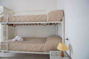 A bunk bed with a quilted mattress, a pair of folded towels, and a bedside lamp on a table. - GuestHost - Golfo Aranci Sunny Retreat Apartment with Terrace! (Golfo Aranci)