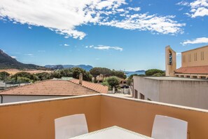 Un balcon avec une table et des chaises, donnant sur un paysage côtier avec des bâtiments et des montagnes.