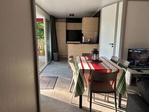 A modern kitchen with wooden cabinets, a dining area with a striped tablecloth, and a TV on a stand. - Homerez - Chalet in Hasparren. (Hasparren)