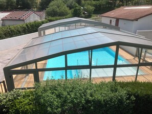 A swimming pool with a glass enclosure, surrounded by greenery and residential buildings. - Homerez - Chalet in Hasparren. (Hasparren)