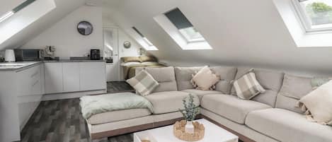 Una habitación tipo buhardilla con sofá, mesa de centro y zona de cocina.