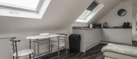 A compact kitchen with a skylight, a small dining area with a table and chairs, and a sofa in a living area.