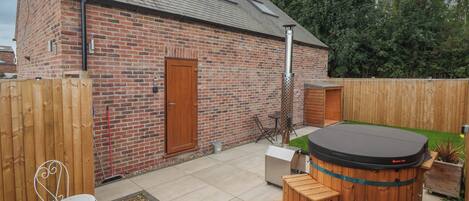 A brick building with a wooden door, a hot tub, and a fenced garden area.