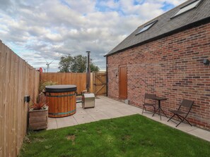 A backyard with a brick building, a wooden fence, a hot tub, and a patio table with chairs. - Fields View (Bridlington)