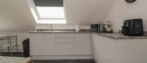 Una cocina compacta con tragaluz, microondas, cafetera y un reloj en la pared.