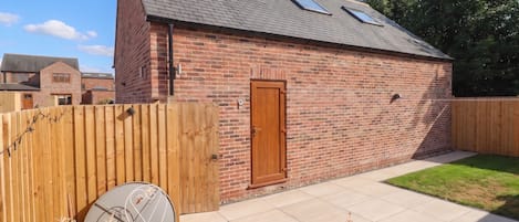 Een bakstenen gebouw met schuine kap, een houten deur en een kleine tuin met omheining.